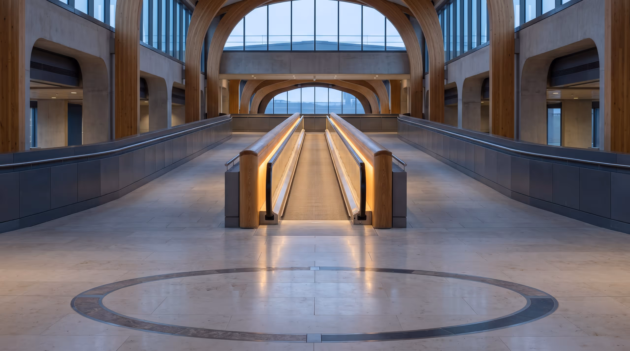 A bright moving walkway runs straight through a transit hall beside open walking routes.